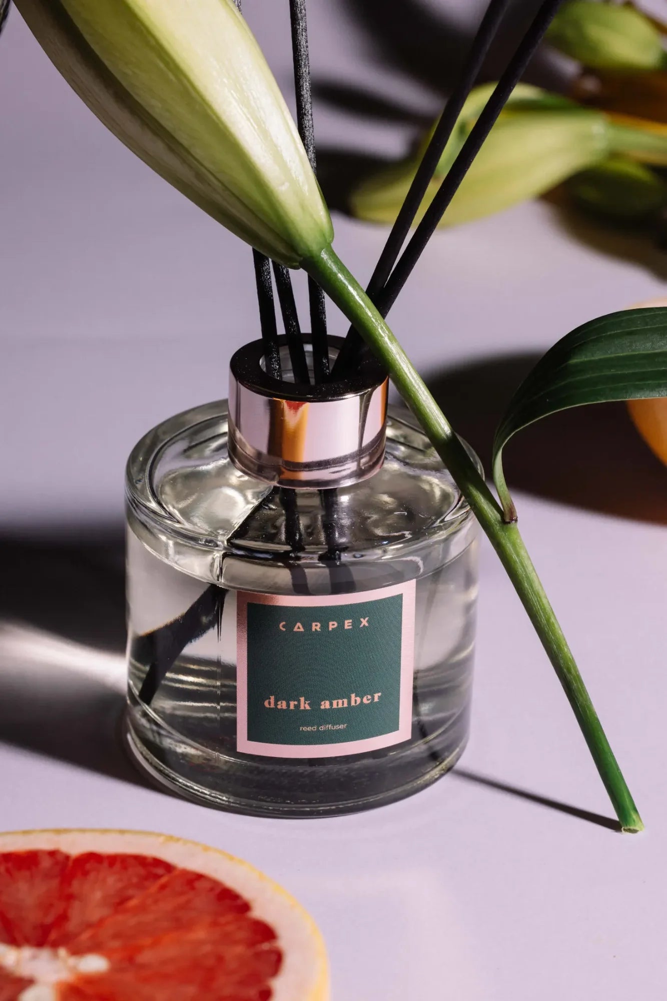 Carpex “Dark Amber” reed diffuser, zarif yeşil yapraklar ve greyfurt detayıyla pastel mor fonda sunulmuş modern ürün çekimi. Pentome Studio’da çekilmiştir.
Carpex “Dark Amber” reed diffuser showcased with elegant green leaves and grapefruit detail on a soft lilac background. Photographed at Pentome Studio.
